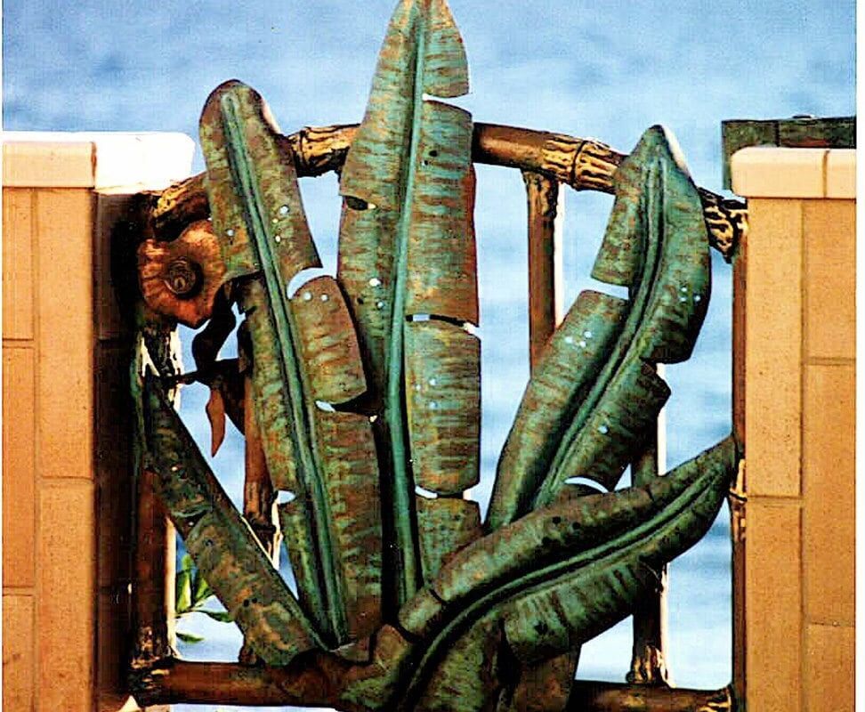 A dog peeking through a gate with large cactus plants in front.
