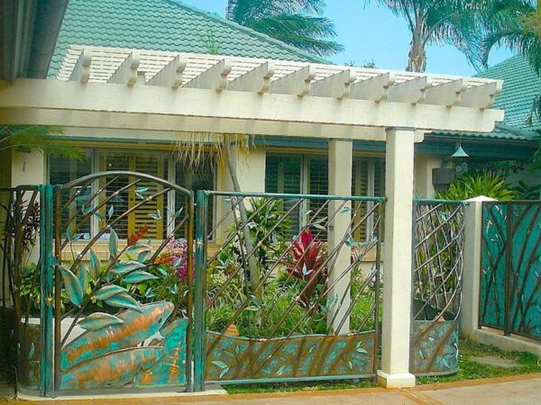 Decorative metal gate with floral design in front of a tropical home.