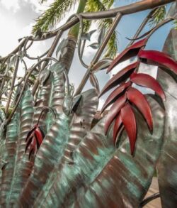 Decorative metal leaves hanging from a tree branch outdoors.