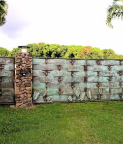 Large metal gate with decorative patterns and stone pillars in a green yard.