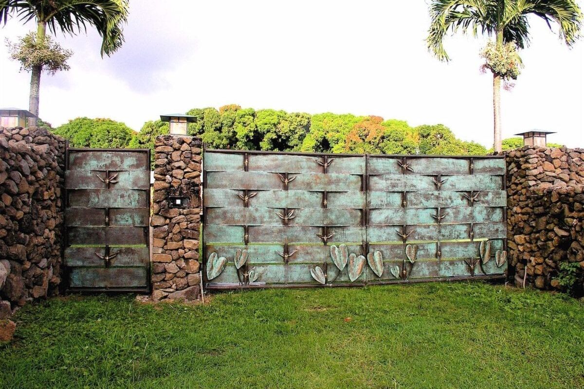 Large metal gate with decorative patterns and stone pillars in a green yard.