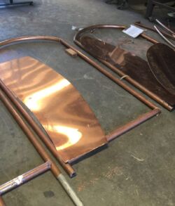 Stenciled banana leaves and round copper framework Two shiny copper fireplace screens with arched tops lying on the floor.