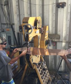 Pounding and shaping of the banana leaf texture and vein work. Two workers operate a large industrial machine inside a workshop.