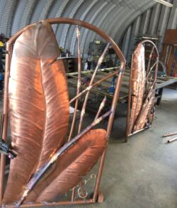 The pedestrian gates taking shape before bamboo leaves and patina Copper feather-shaped metal sculptures in a workshop.