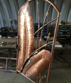 The pedestrian gates taking shape before bamboo leaves and patina Large industrial copper pipes and coils in a workshop.