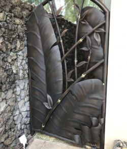 Decorative metal gate with intricate leaf designs and a stone wall.
