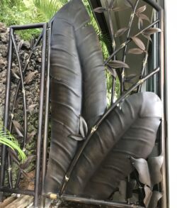 Side Pedestrian Gate Large green leaves growing near a metal fence.