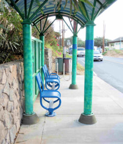 Blue benches and green pillars line a quiet outdoor sidewalk.