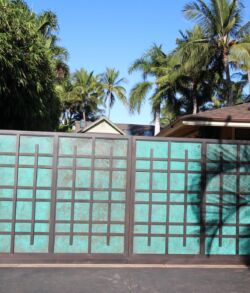 A tall green gate with a grid pattern in front of palm trees and houses.