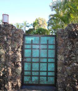 A turquoise metal gate set between rustic stone walls under a sunny sky.