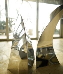 Stainless steel table base close up Close-up of two shiny, metallic, curved sculptures on a wooden surface.