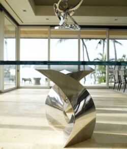 Stainless steel table base end view Shiny modern metal sculpture with a whale tail design in a bright room.