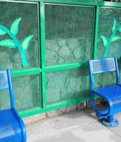 Blue metal benches lined up beside a green mesh fence with painted leaves.