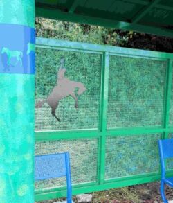 A green-painted fence with a horse silhouette cutout under a covered structure.