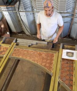Man working on a detailed wooden project inside a workshop.