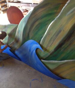 Ian Padilla adding the finishing touches of patina A man painting a large, colorful sculpture outdoors.