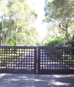 A closed metal gate blocking a path surrounded by trees.