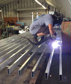 Worker welding metal beams in an industrial setting.
