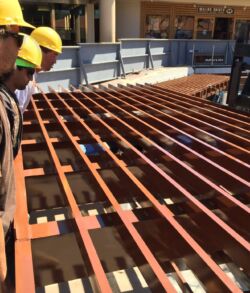 Workers inspecting wooden beams on a construction site deck.