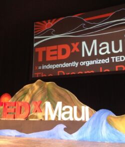 Full stage view TEDxMaui event stage with logo and tropical-themed decor.
