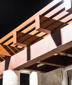 Modern wooden pergola casting shadows on a building exterior at night.