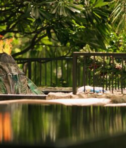 Madam Pele's copper volcano A serene outdoor pool surrounded by lush greenery and a rock waterfall feature.