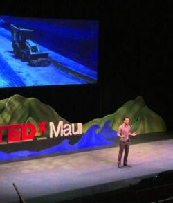 Sean Connelly guest speaker- recovering the technology of paradise Speaker presenting at TEDxMaui event on stage with screen above.