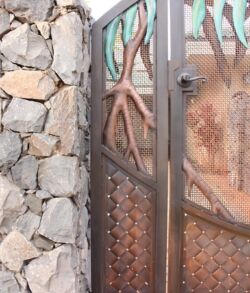 Detail close up of Hala gate side panel Artistic metal door with natural branch and honeycomb designs beside a stone wall.