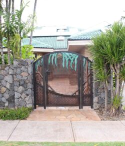 Copper Hala tree entrance gate Stone wall with metal gate entrance and tropical plants.
