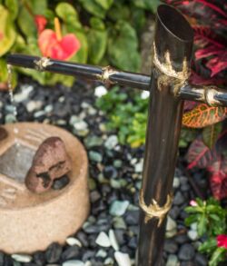A bamboo water fountain with a butterfly and a stone in a garden.