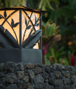 Copper and brass Bamboo and banana leaf column lamp Decorative outdoor lantern on volcanic rock with a leafy background.