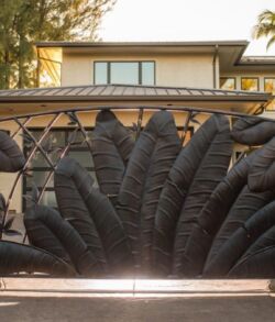 Black metal gate with intricate feather-like designs at a residential entrance.