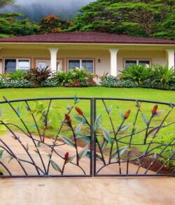 Red ginger and sculpted copper and brass bamboo main entrance gate Ornate metal gate in front of a charming house with lush green lawn.