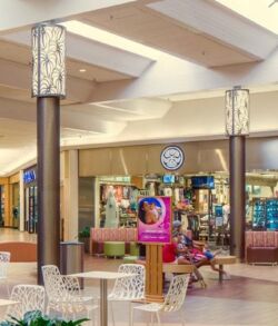 Aluminum column lighting at Prince Kuhio shopping center Hawaii Island Indoor mall scene with a clock and store displays.