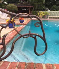 Close up view of "Ubuntu Metal bird sculpture overlooking a backyard pool.