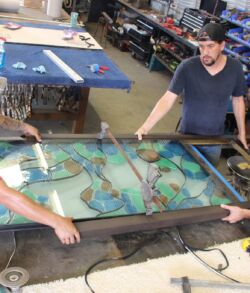 Three men working on a large stained glass window in a workshop.