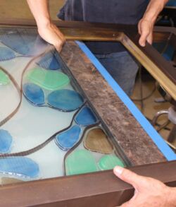 Hands assembling stained glass with lead came strips.