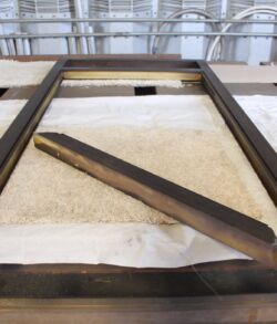 Wooden frame with white fabric and a wooden stick inside, placed on a surface.