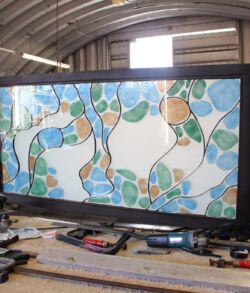 Large decorative glass panel with an intricate tree design in a workshop.