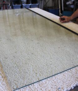 A hand placing a glass sheet on a carpeted floor.
