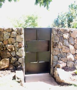 Full view of utility access gate A modern metal gate set in a rustic stone wall under bright sunlight.