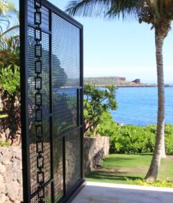 A decorative metal gate opens to a lush garden by the ocean.