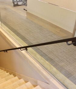 Full view of interior staircase handrail Black handrail alongside stairs with glass panel on the side.