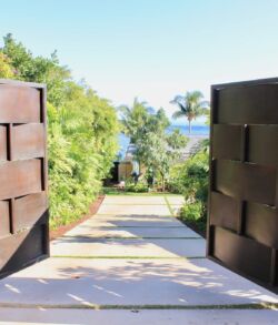 Open wooden gates revealing a path to a garden and ocean view.