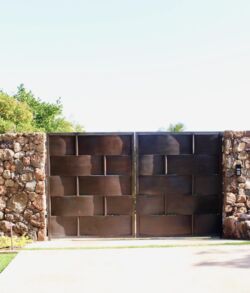 Full view of main entrance gate Sturdy metal gate set in a stone wall with greenery above.