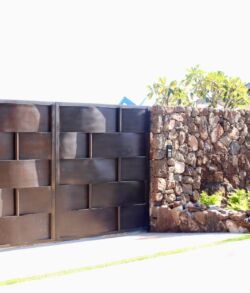 Main entrance gate and pedestrian entry gate A modern dark concrete and stone wall fence under bright sunlight.