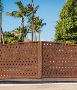 Full view of corten steel entrance gate Brown wooden gate with lattice design in a sunny residential area.