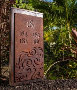 Decorative metal address plaque with house numbers in a garden.