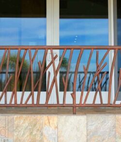 Padilla Designs signature copper sculpted Kiawe wood banister Balcony railing with a view of furniture and a sky reflection on glass doors.