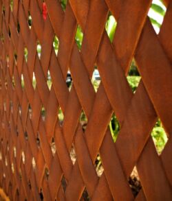 Close up details of a custom corten steel entrance gate Close-up of a wooden lattice fence with sunlight filtering through.